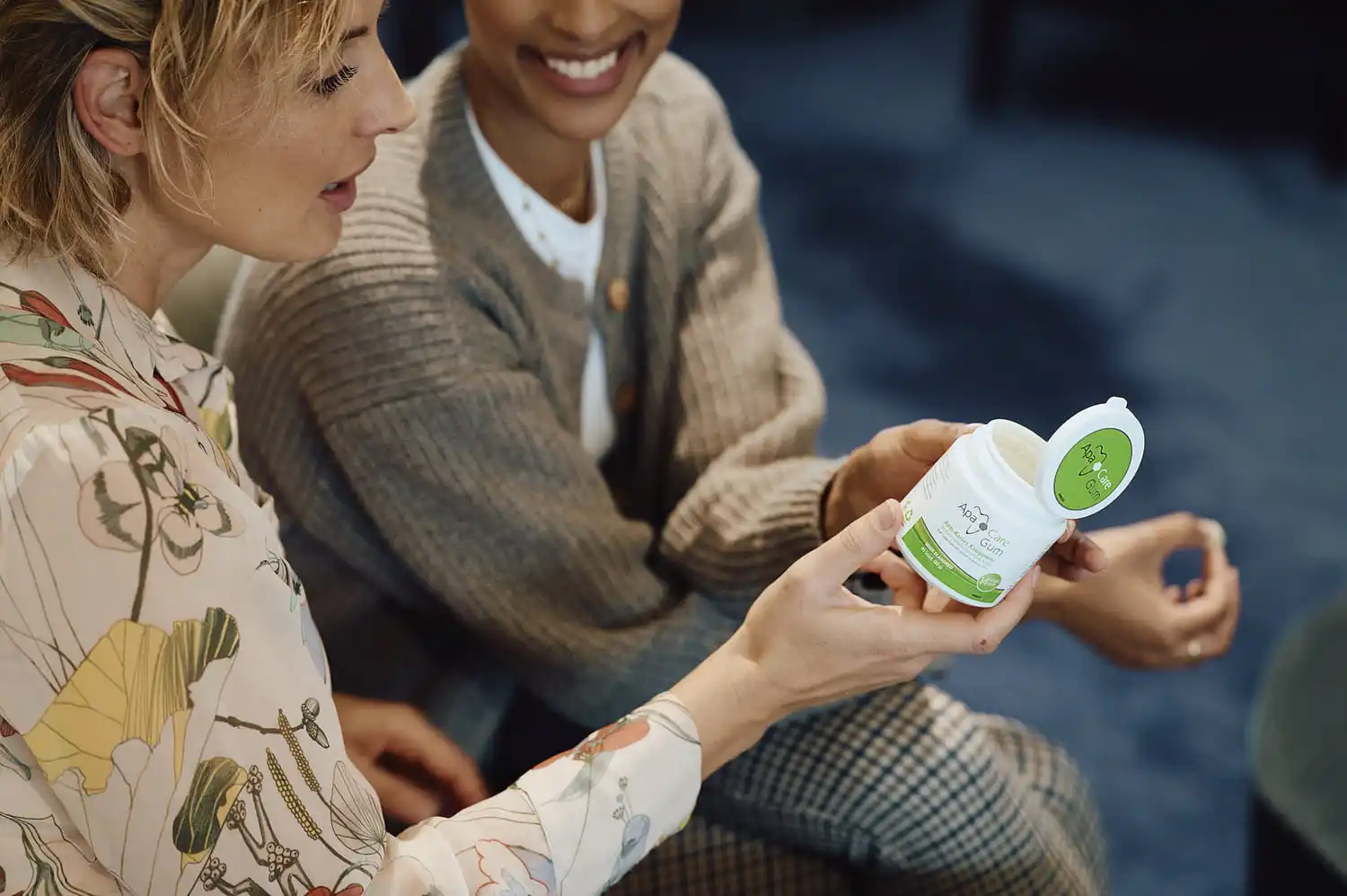 Zwei Frauen schauen auf eine geöffnete Kaugummi-Dose mit ApaCare Anti-karies-Kaugummis